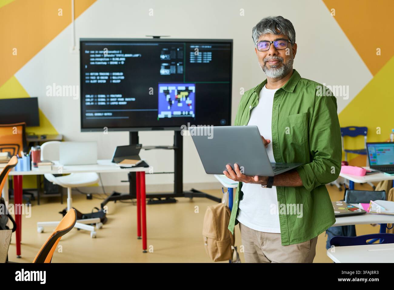 Portrait of Indian Middle Aged IT Teacher Holding Laptop in Classroom Stock Photo