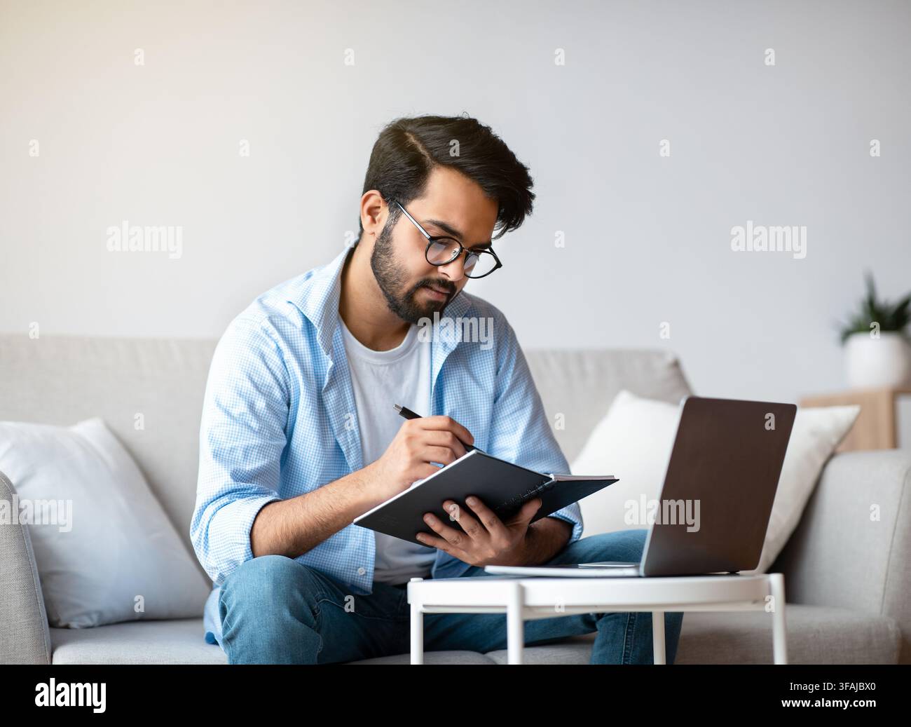Young Arab Freelancer Man Taking Notes And Working On Laptop At Home Stock Photo