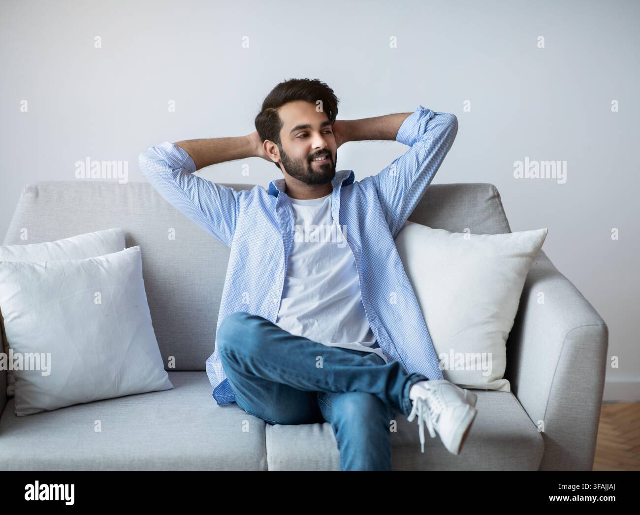 Relaxed Arab Guy Leaning Back On Couch With Hands Behind Head Stock Photo
