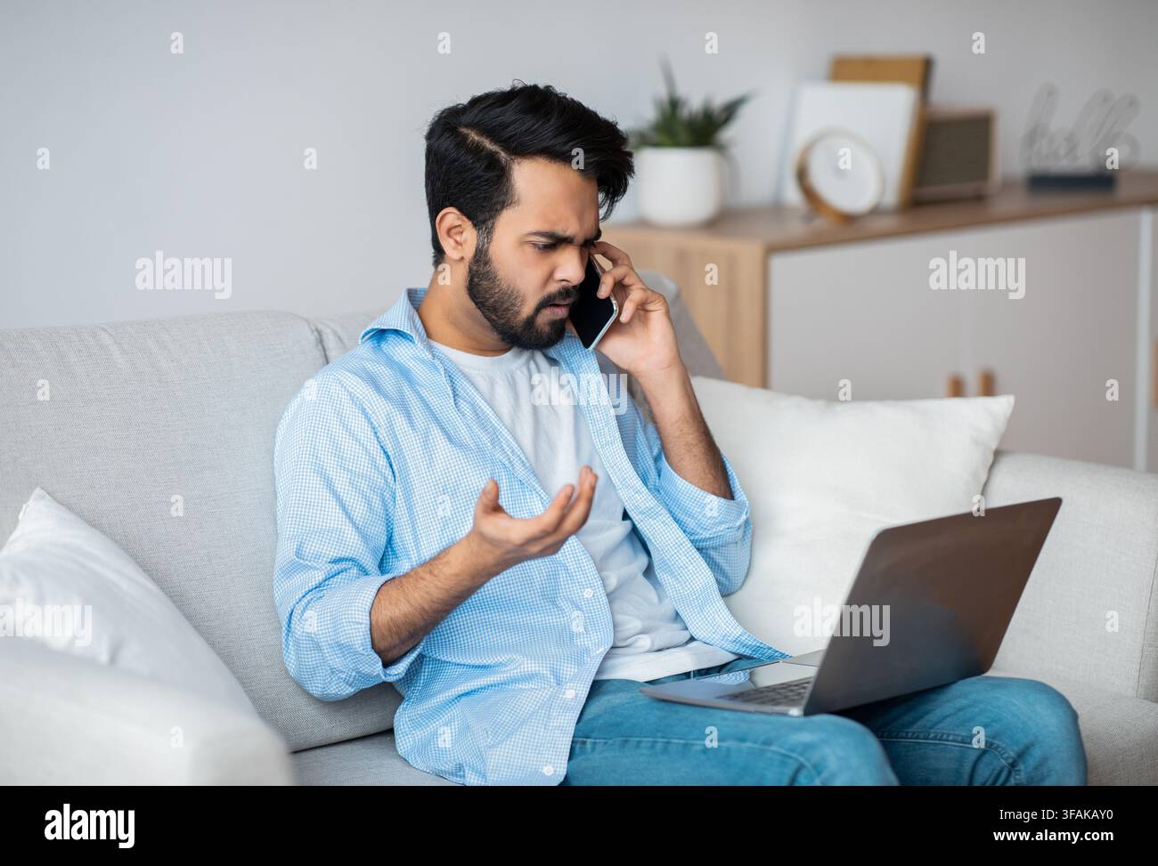 Computer Problems. Frustrated arab guy using cellphone and looking on laptop screen Stock Photo