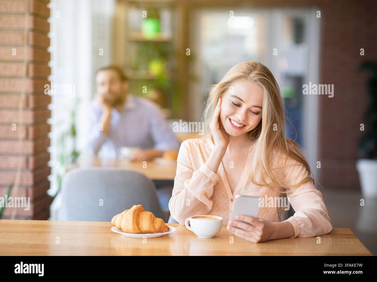 Beautiful young woman using smartphone during breakfast at cafe, young guy looking at her, empty space Stock Photo