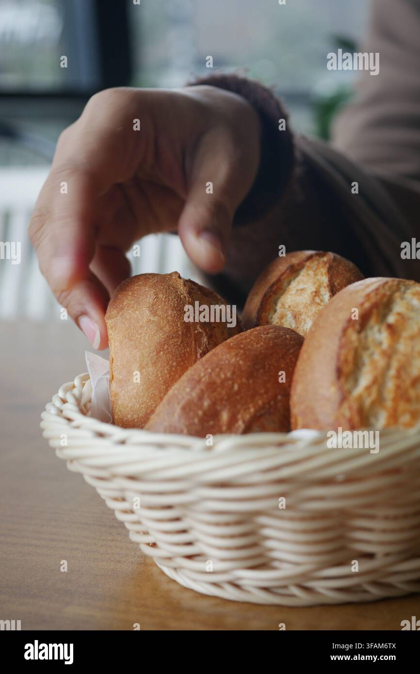 Hand reaching for bread rolls in a basket Stock Photo