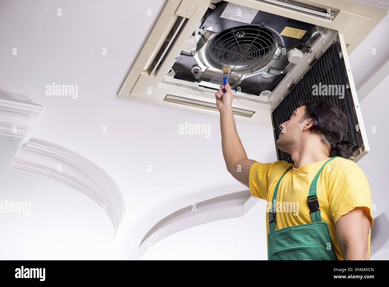Young mechanic repairs ceiling air conditioner Stock Photo