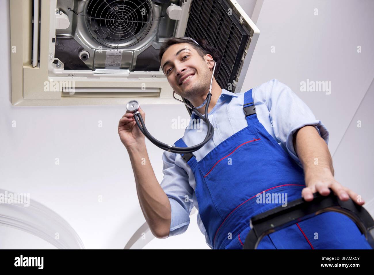Young mechanic repairs ceiling air conditioner Stock Photo