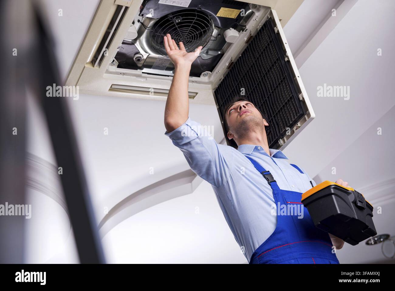 Young mechanic repairs ceiling air conditioner Stock Photo
