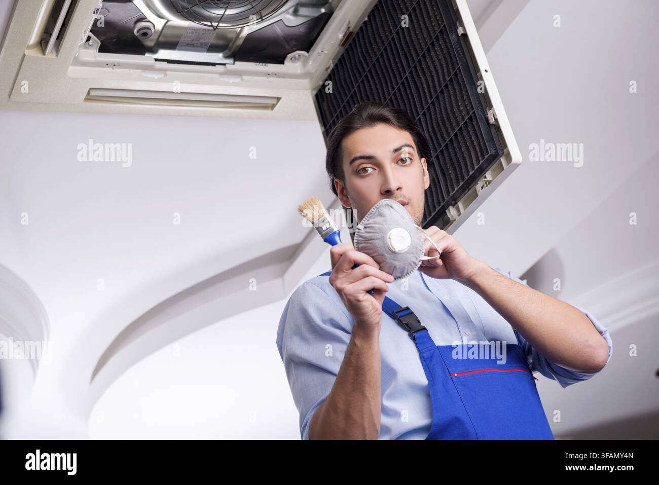Young mechanic repairs ceiling air conditioner Stock Photo
