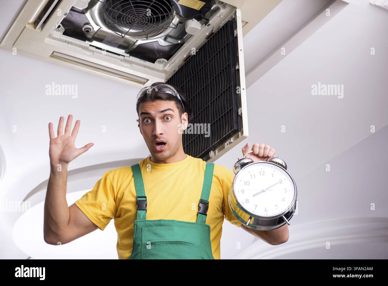 Young mechanic repairs ceiling air conditioner Stock Photo