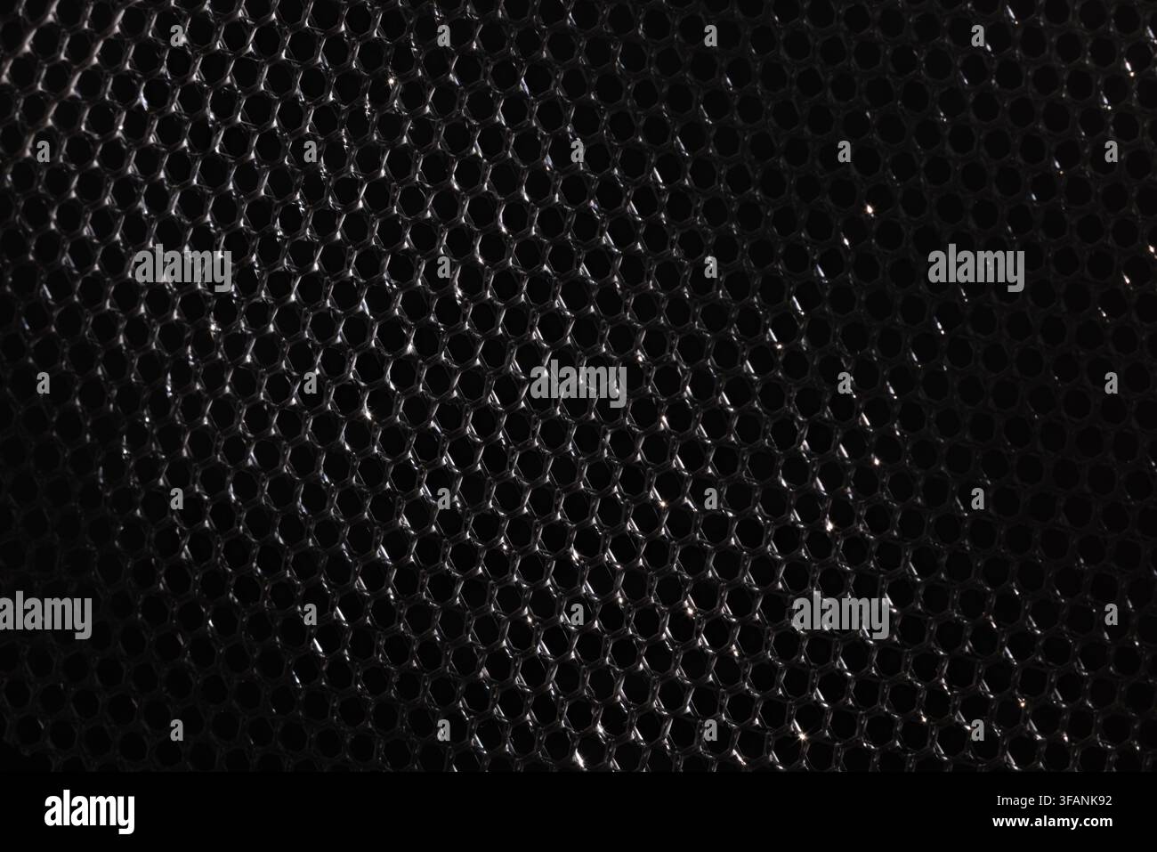 Dark black metallic mesh with subtle silver reflections and repeating hexagonal pattern for moody industrial texture background Stock Photo