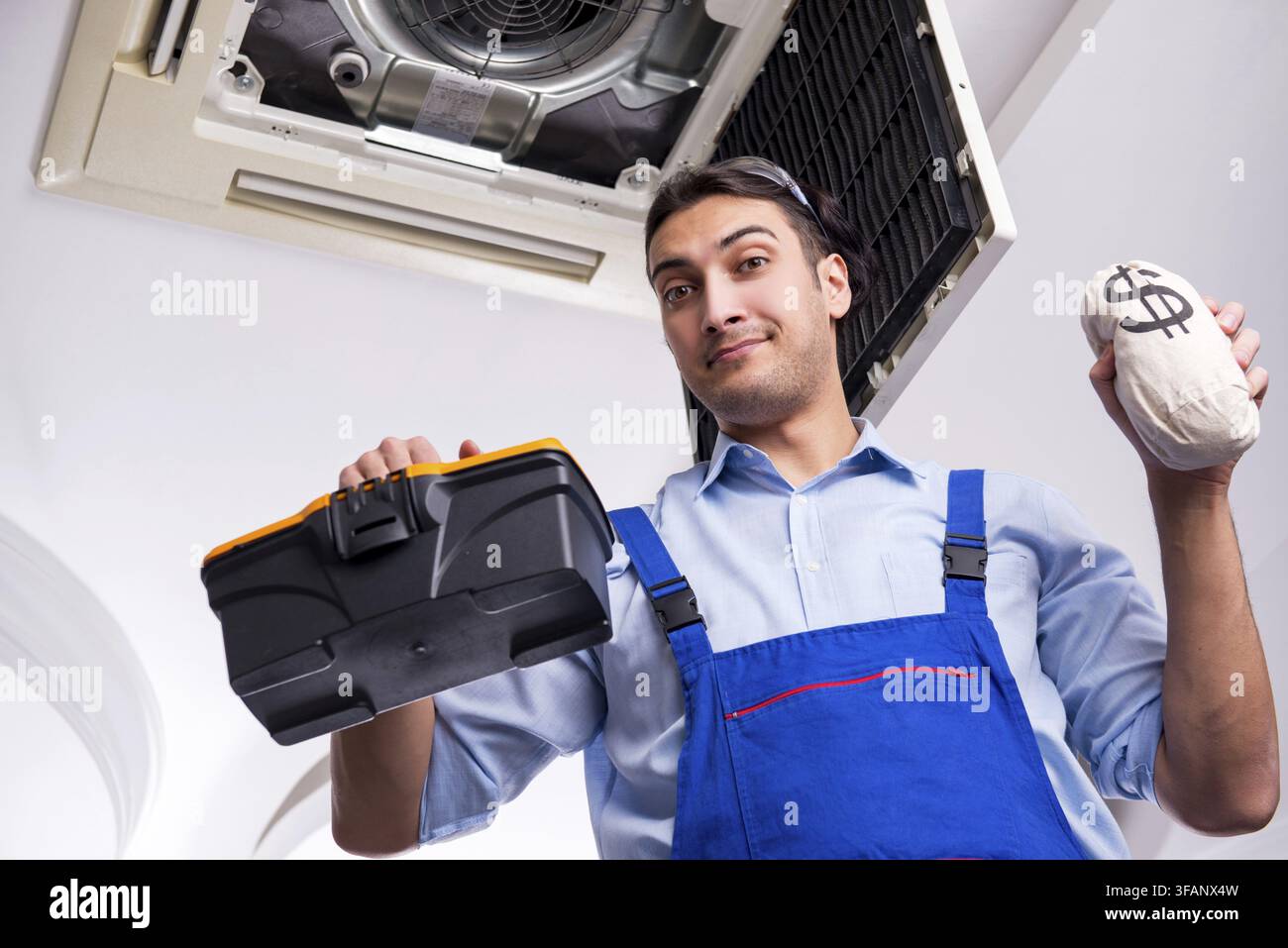 Young mechanic repairs ceiling air conditioner Stock Photo