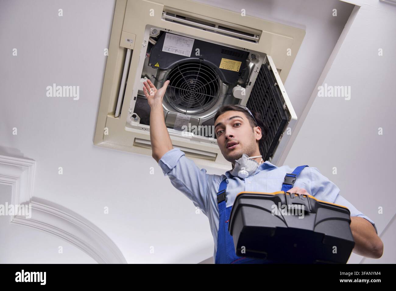 Young mechanic repairs ceiling air conditioner Stock Photo