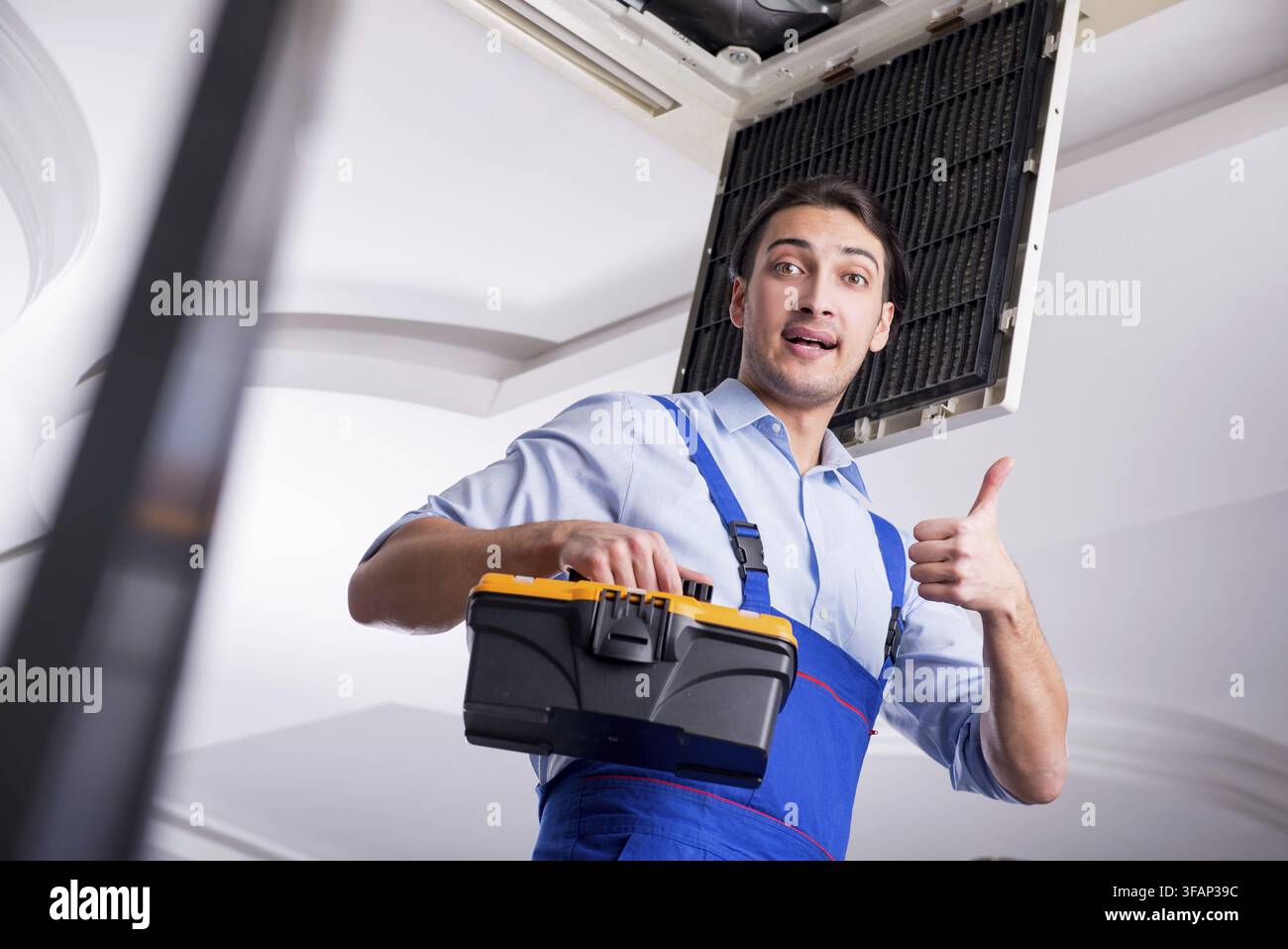 Young mechanic repairs ceiling air conditioner Stock Photo