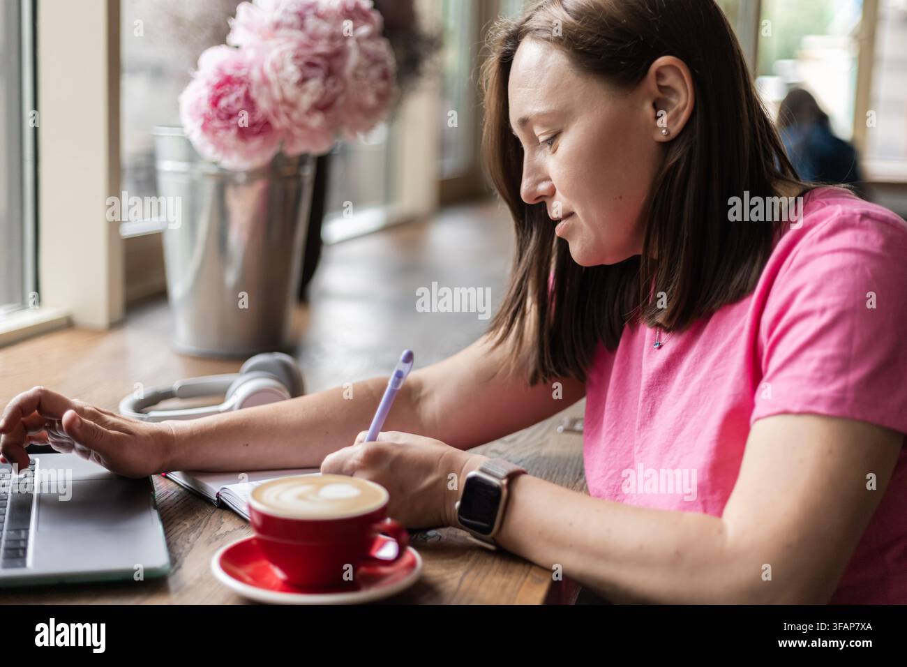Woman working on laptop with coffee and notebook in cafe Stock Photo