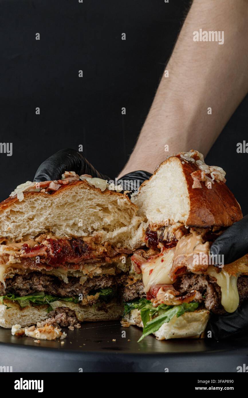 Hands in gloves hold a huge messy burger cut open Stock Photo