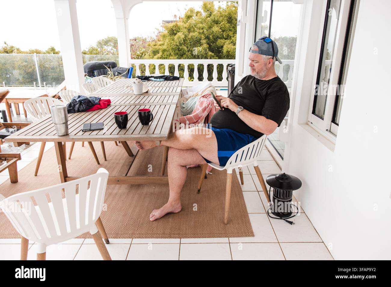 Middle aged man relaxes on porch using phone Stock Photo