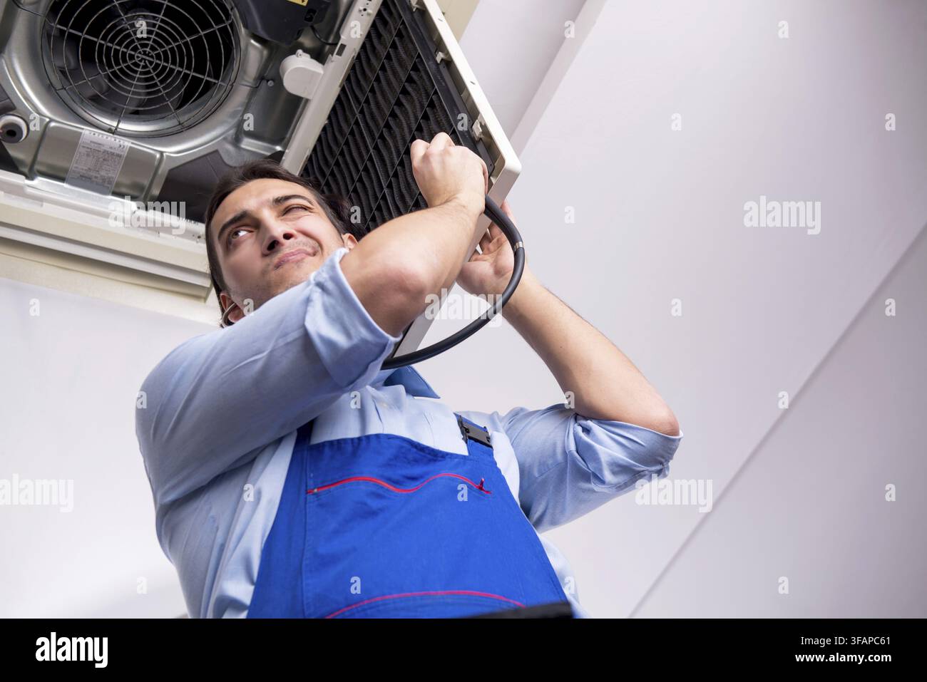 Young mechanic repairs ceiling air conditioner Stock Photo