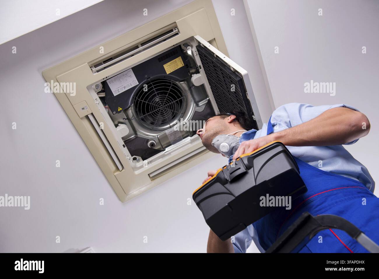 Young mechanic repairs ceiling air conditioner Stock Photo
