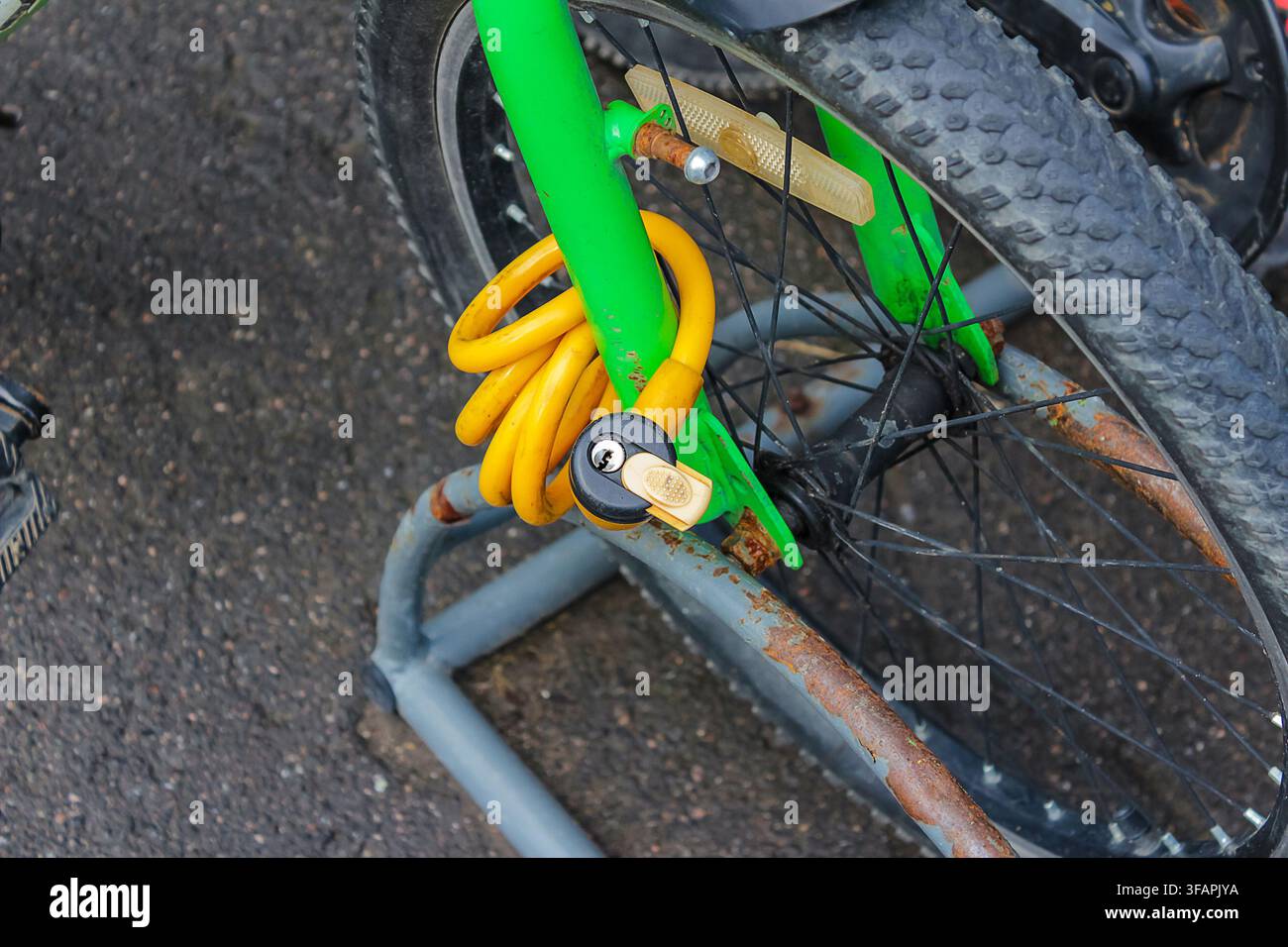 A partial view of a bicycle secured to a metal stand with a yellow curved lock. Focus is on the frame, lock, and part of the wheel Stock Photo