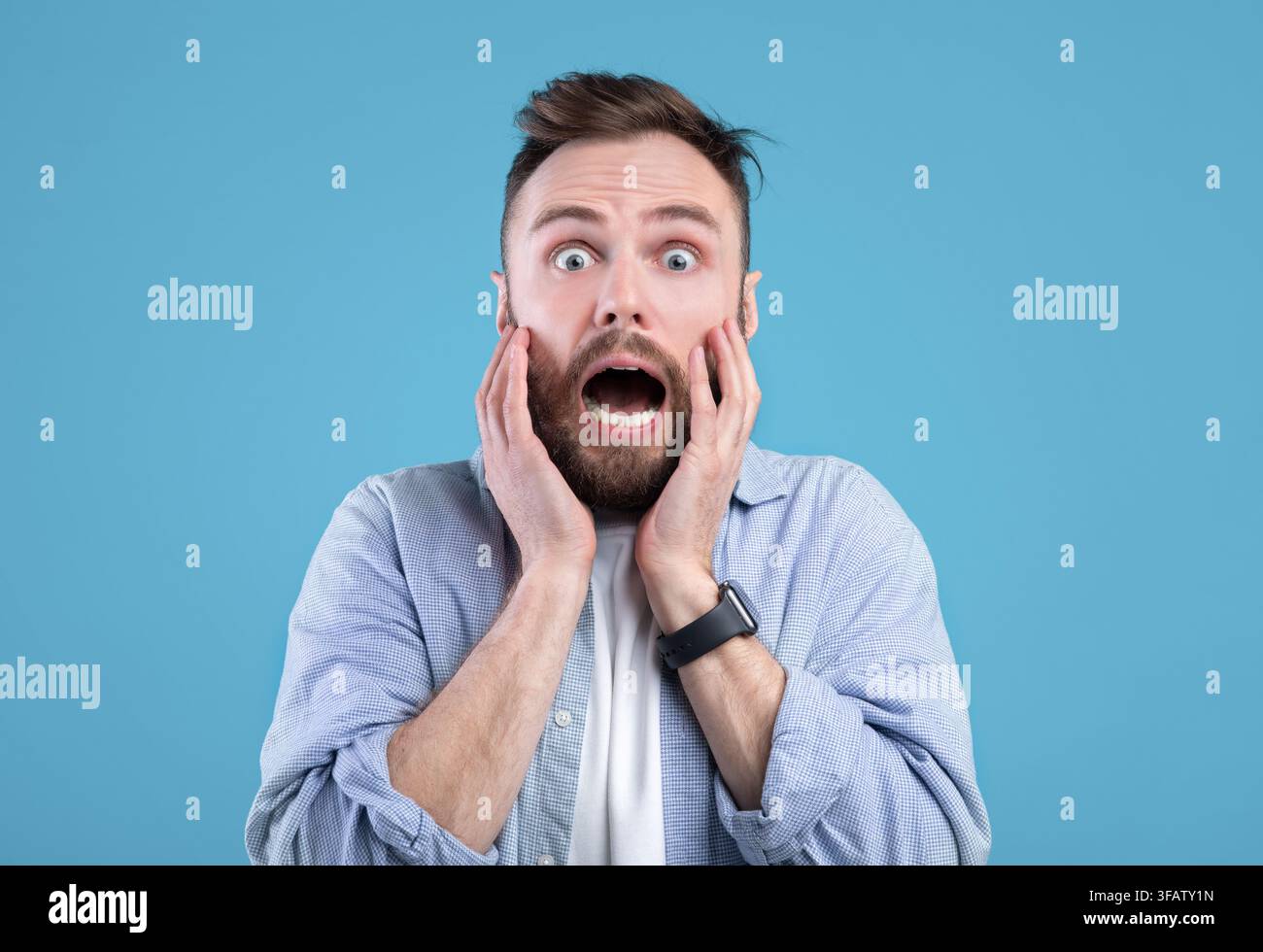 Scared young guy screaming in panic over blue studio background Stock Photo