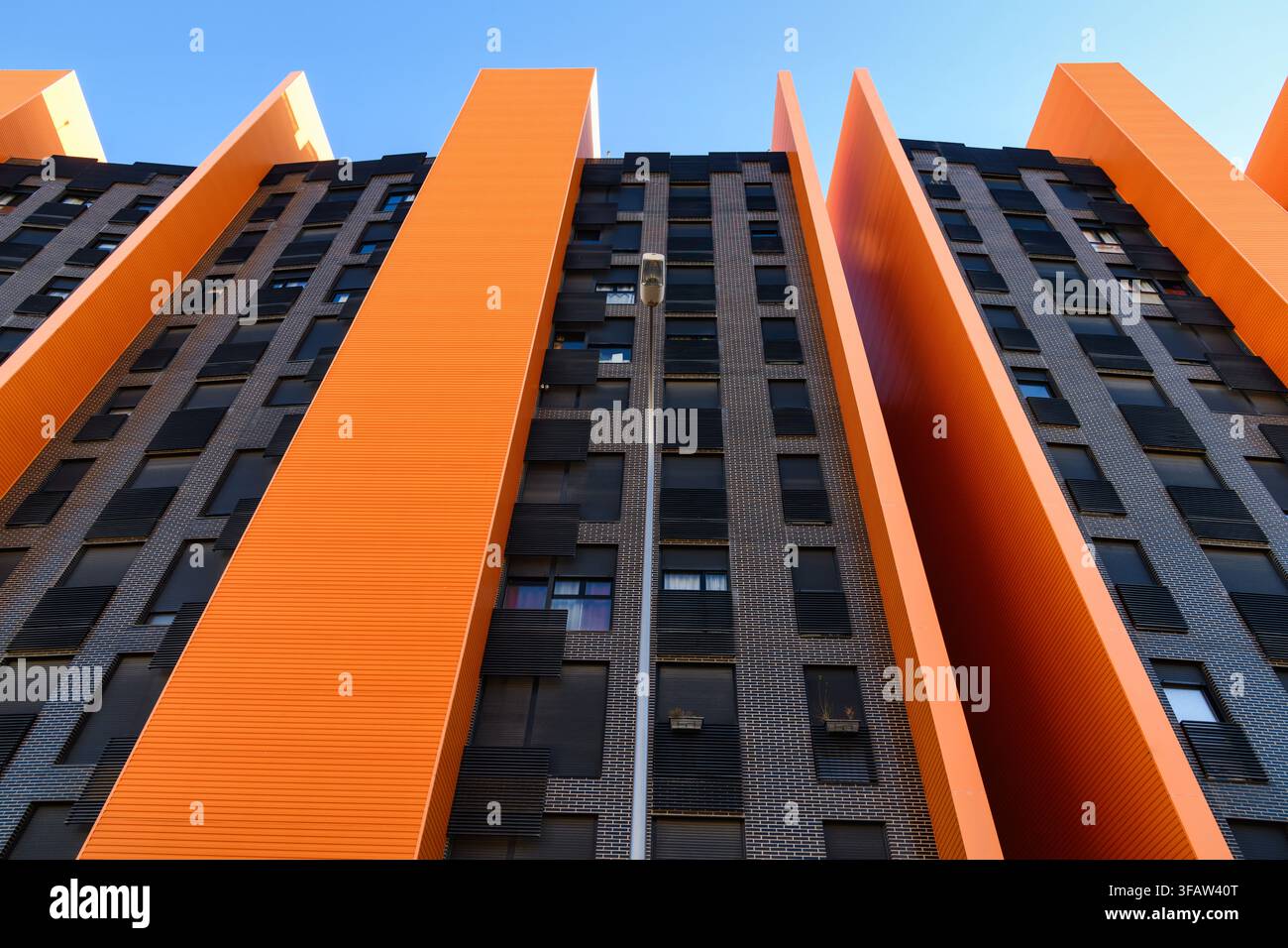 Low-angle view of a modern high-rise building with dramatic orange vertical fins alternating with dark brick facade sections, rising against a clear b Stock Photo