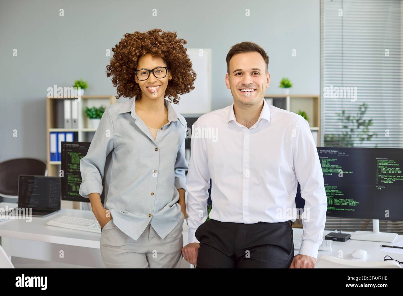 Smiling software developers team portrait in modern office with code on monitors Stock Photo