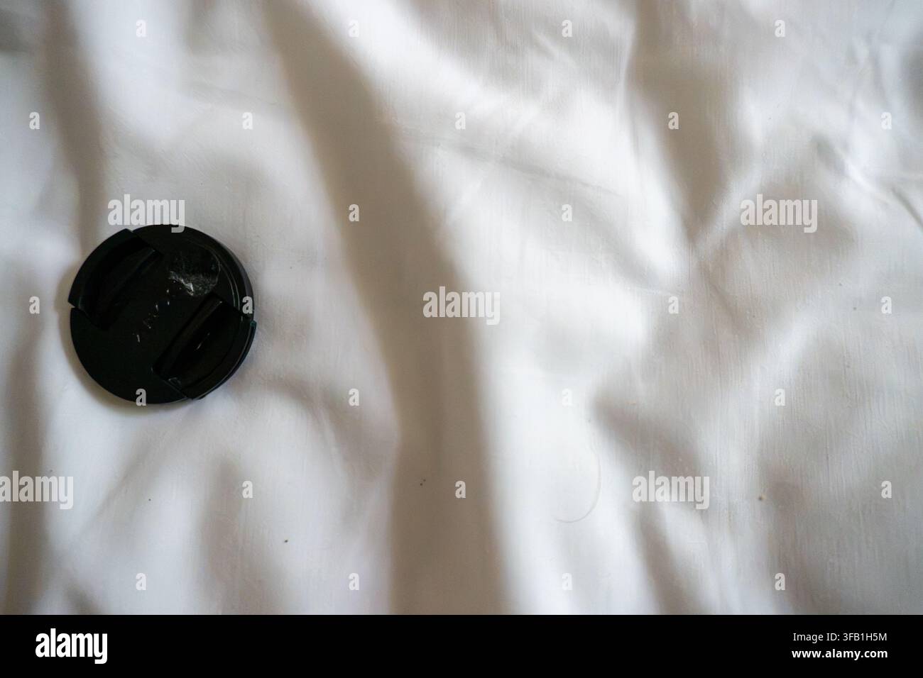 Camera lens cap resting on white fabric surface. Stock Photo