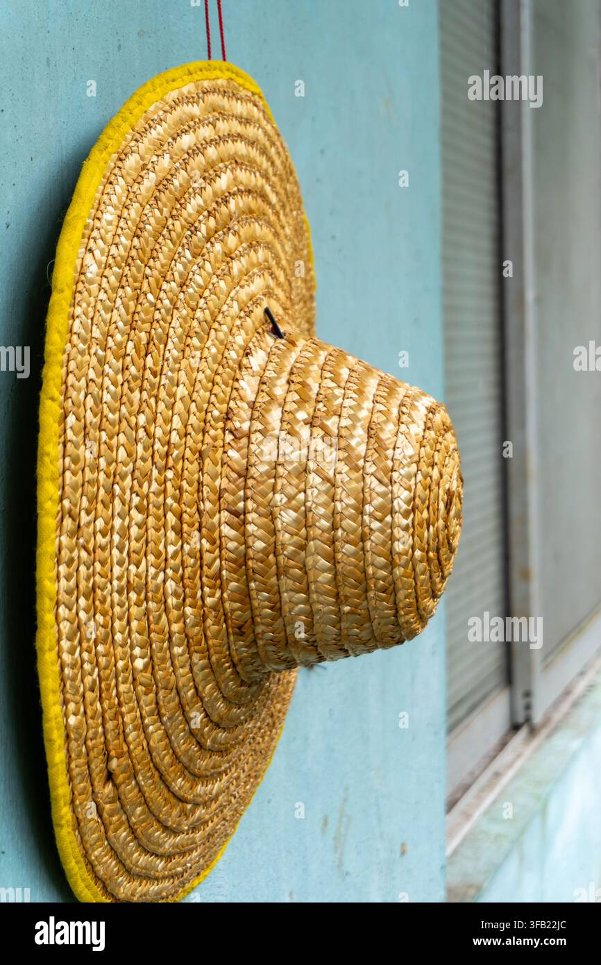 Straw hat hanging on light blue wall exterior. Stock Photo