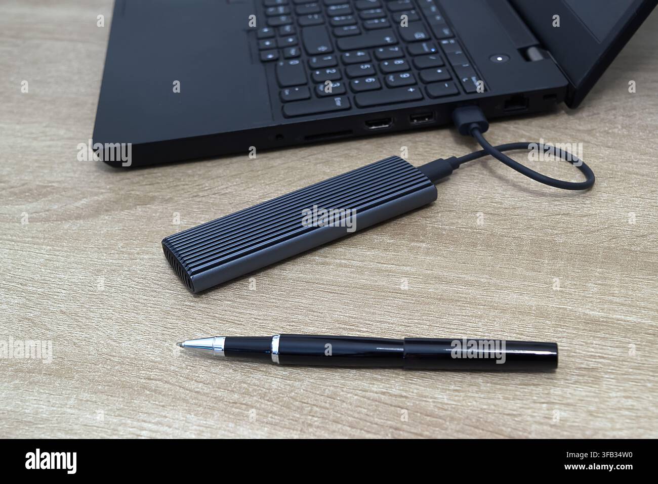 Close-up shot of a modern ribbed grey aluminum external M.2 NVMe SSD enclosure connected via USB-C cable to a black laptop, accompanied by an elegant Stock Photo