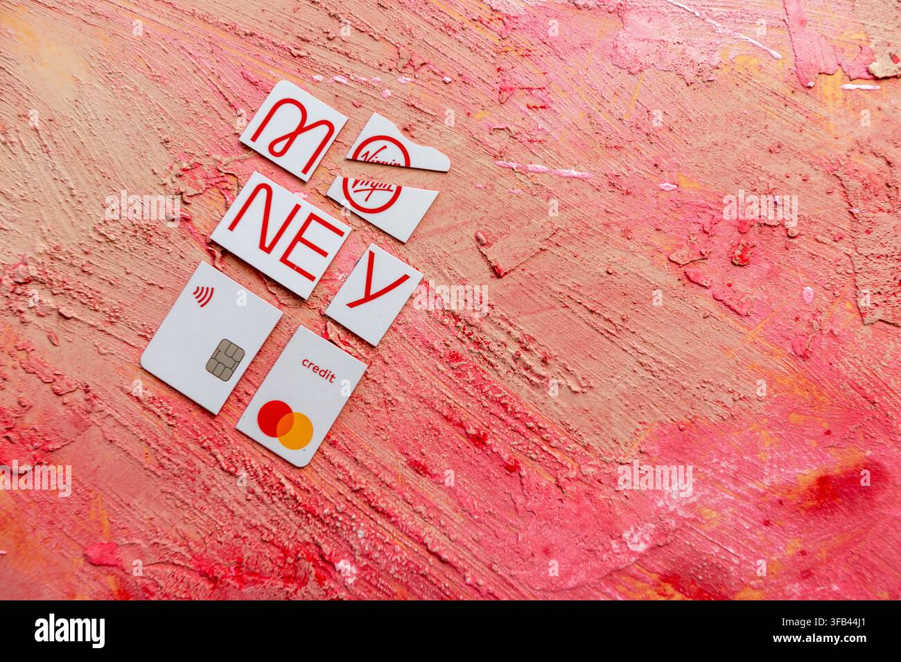 Against a textured red background a Virgin Money Mastercard credit card has been cut in to pieces perhaps too enthusiastically but tidily arranged. Stock Photo