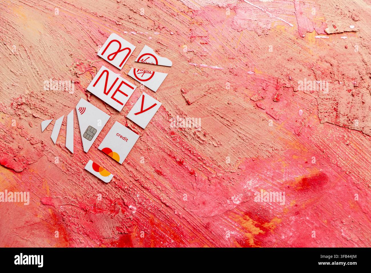 Against a textured red background a Virgin Money Mastercard credit card has been cut in to pieces perhaps too enthusiastically but tidily arranged. Stock Photo