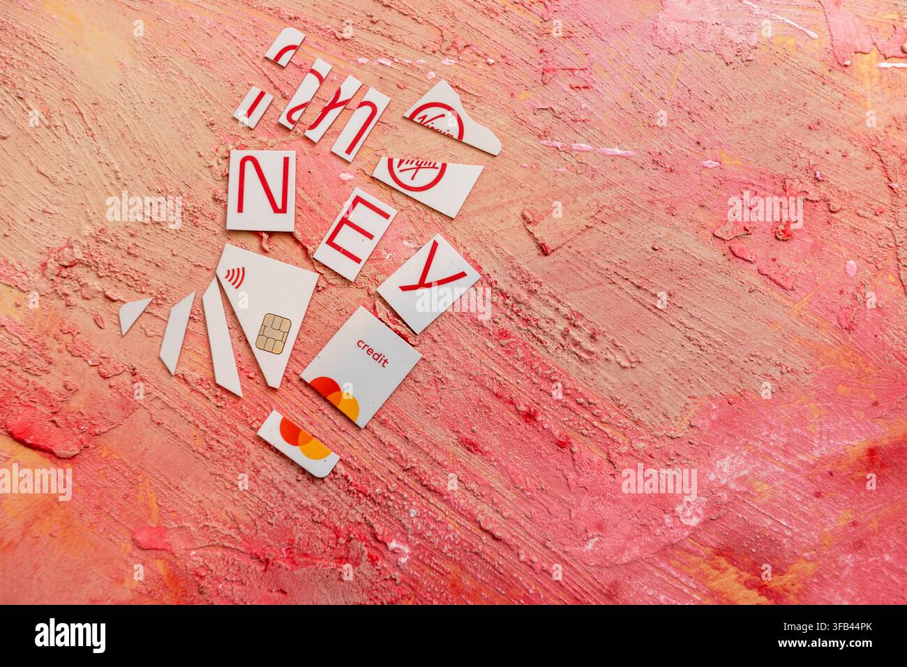 Against a textured red background a Virgin Money Mastercard credit card has been cut in to pieces perhaps too enthusiastically but tidily arranged. Stock Photo