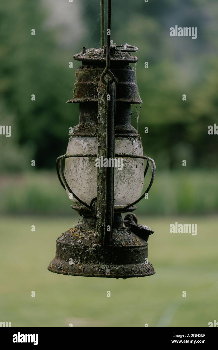 Heavily rusted antique kerosene lantern covered with moss, lichen and cobwebs hanging outdoors Stock Photo