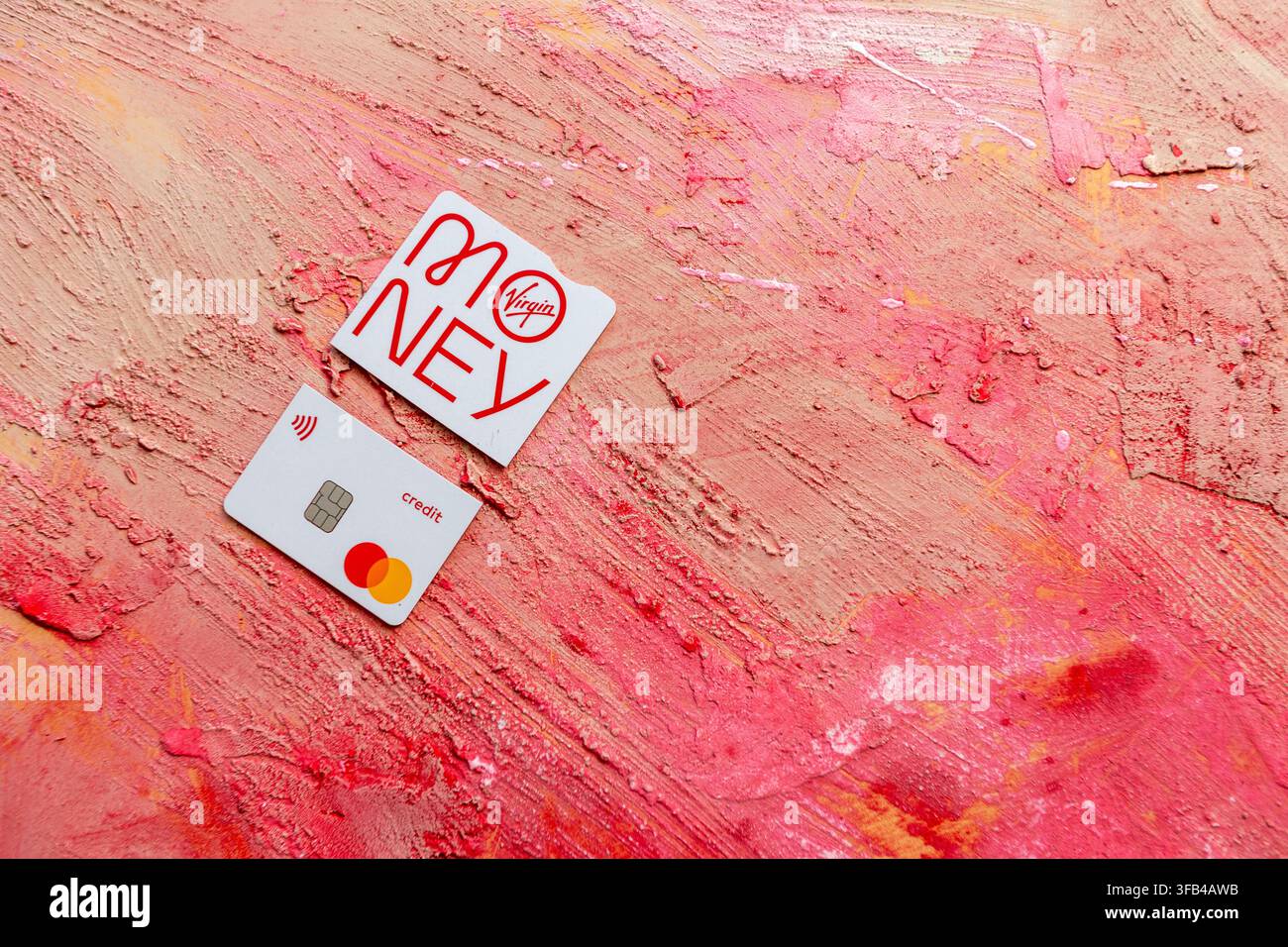 Against a textured red background a Virgin Money Mastercard credit card has been cut in to pieces perhaps too enthusiastically but tidily arranged. Stock Photo