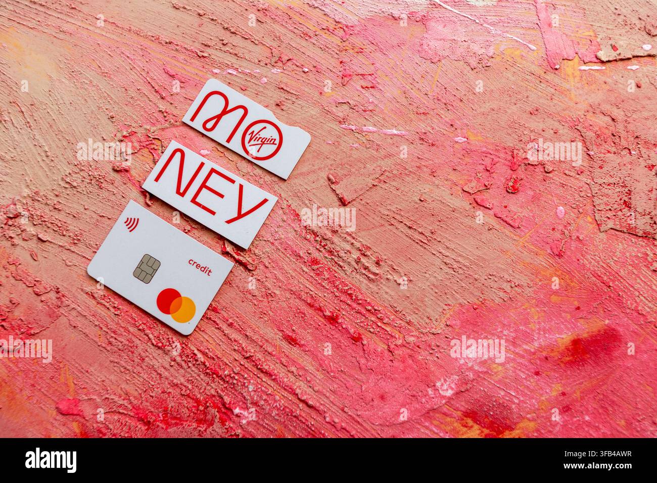 Against a textured red background a Virgin Money Mastercard credit card has been cut in to pieces perhaps too enthusiastically but tidily arranged. Stock Photo