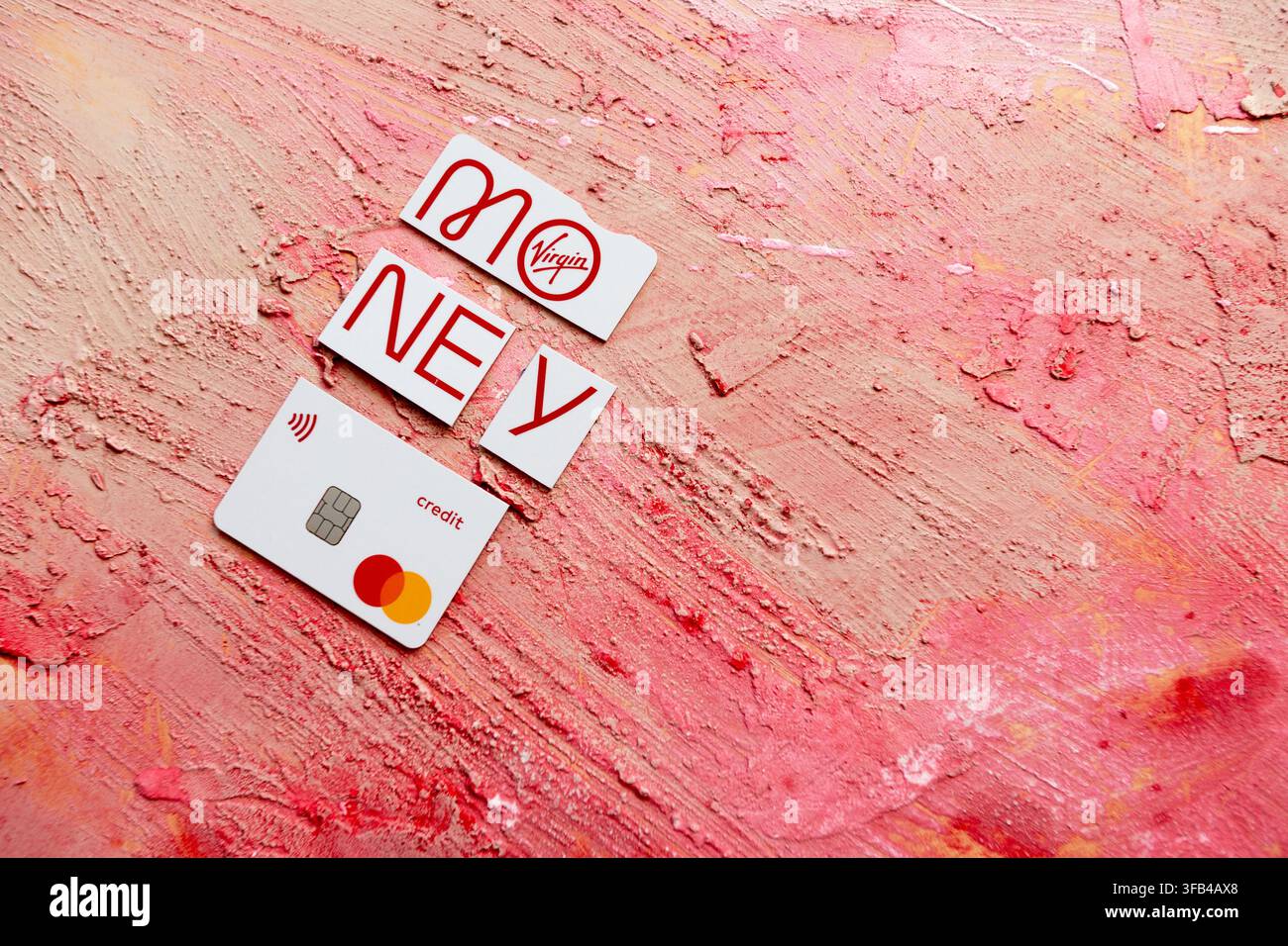 Against a textured red background a Virgin Money Mastercard credit card has been cut in to pieces perhaps too enthusiastically but tidily arranged. Stock Photo