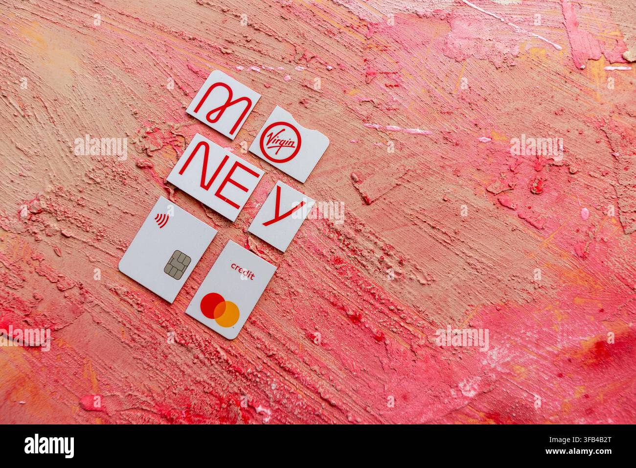 Against a textured red background a Virgin Money Mastercard credit card has been cut in to pieces perhaps too enthusiastically but tidily arranged. Stock Photo