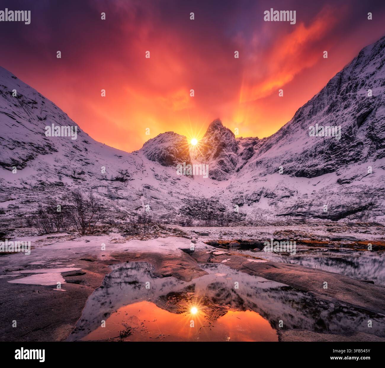 Dramatic red sunset sky over snow covered mountains in Lofoten Stock Photo