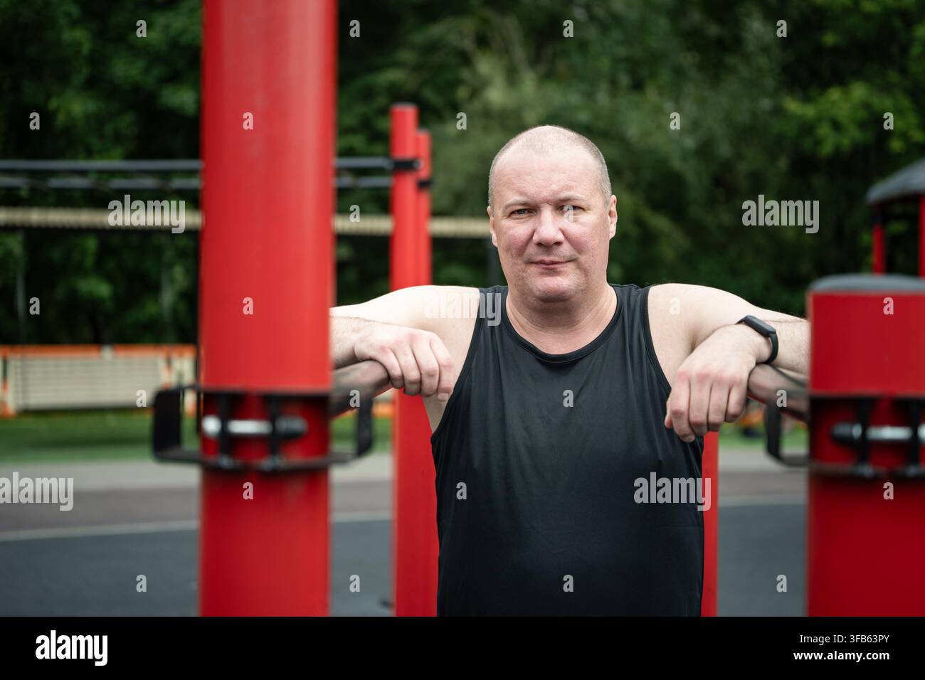 Mature caucasian man resting between exercises on parallel bars at outdoor fitness area, active aging, workout recovery and healthy lifestyle concept. Stock Photo