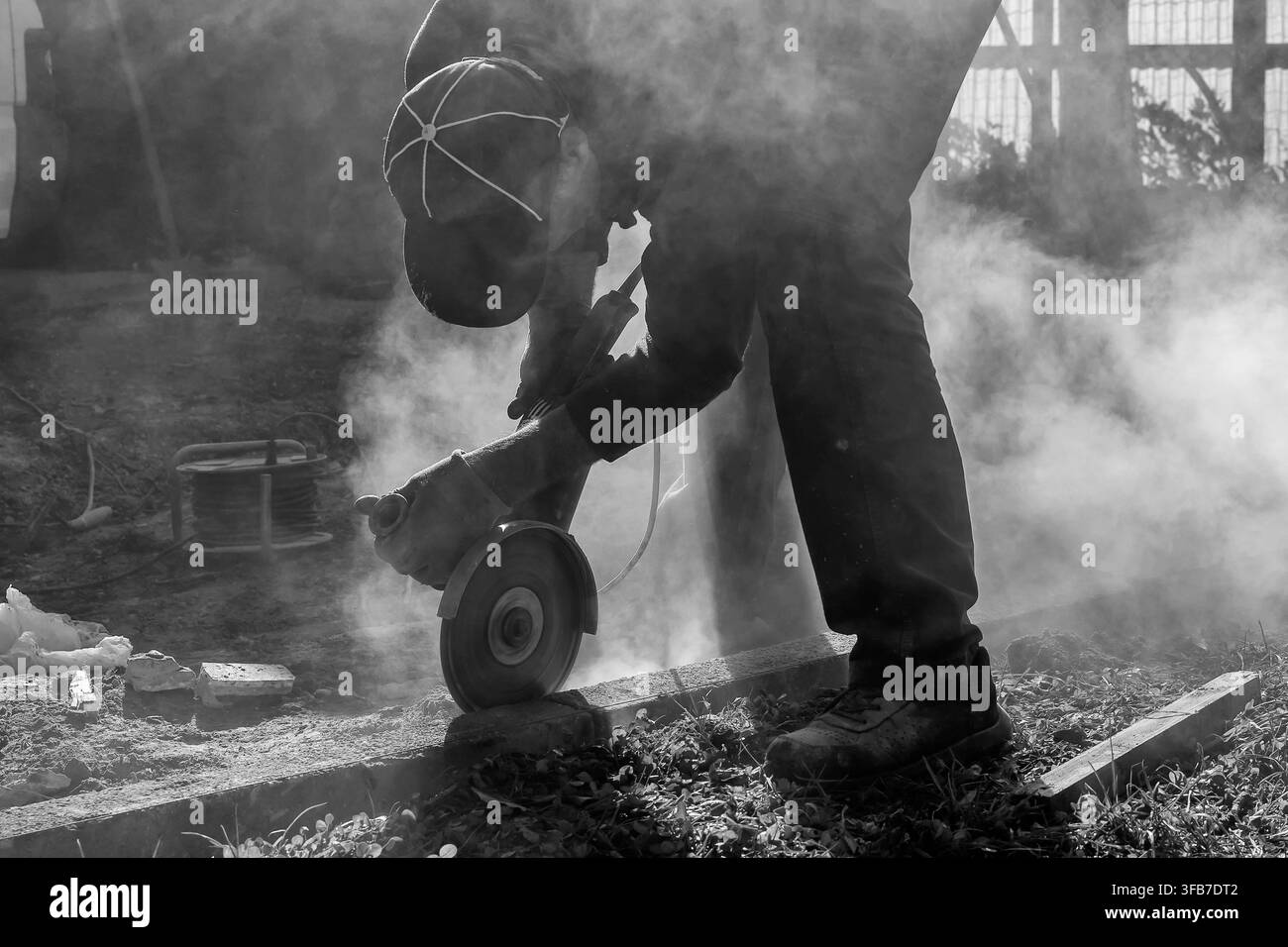 A worker builds a curb using various tools, including an angle grinder, in black and white Stock Photo