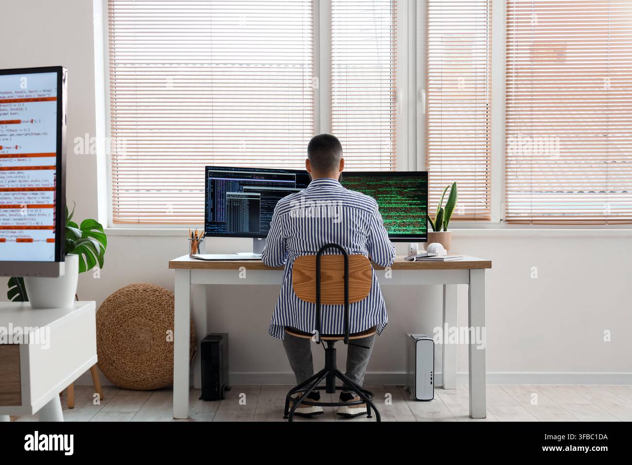 Software development and coding, man working on multiple computer screens with programming code in a modern home office Stock Photo