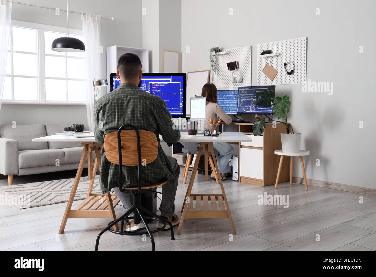 Remote work and software development, two people coding on computers in a modern home office environment Stock Photo
