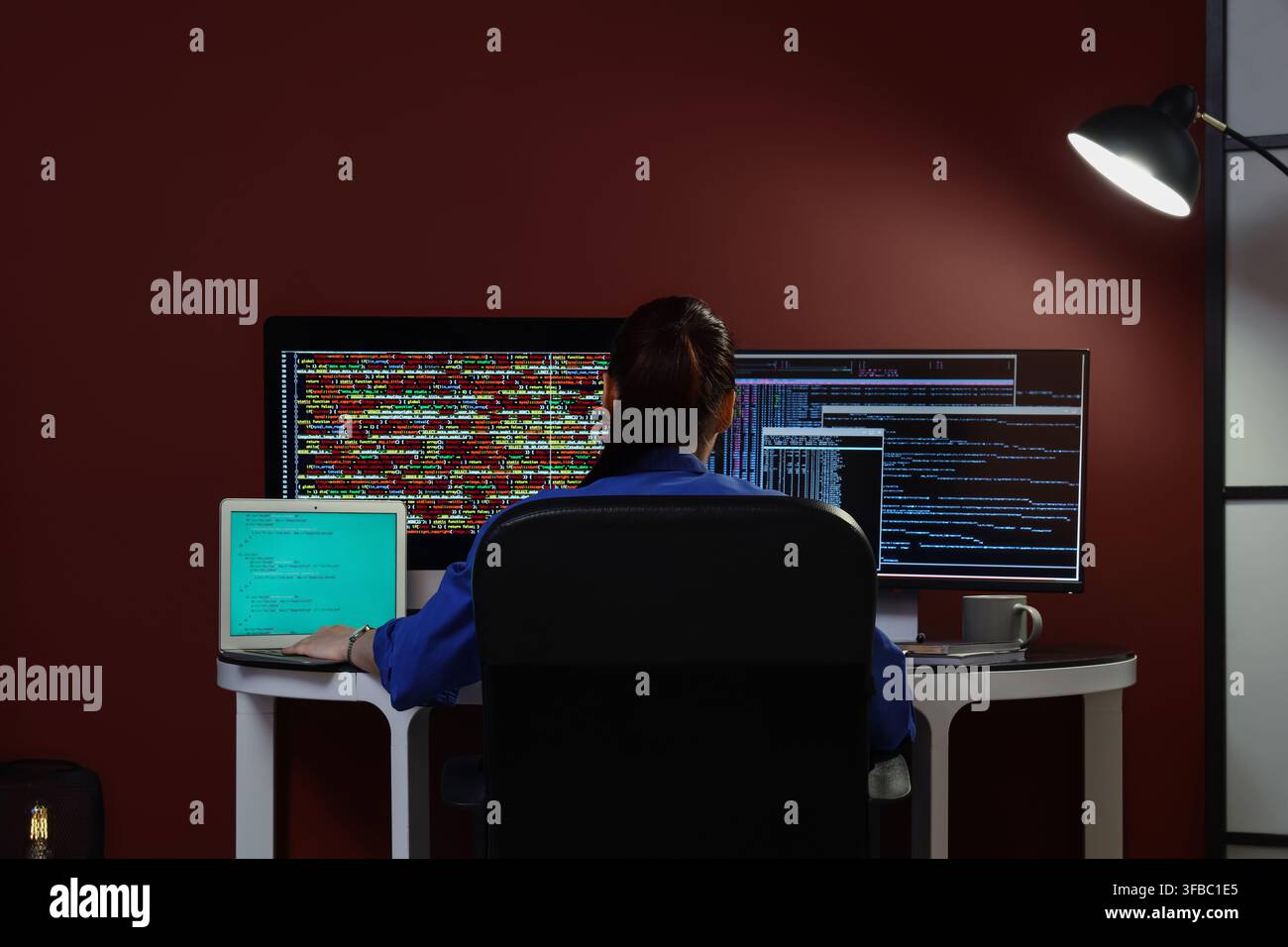 Software development and coding, woman programmer working late on multiple screens with complex code in a dark office Stock Photo