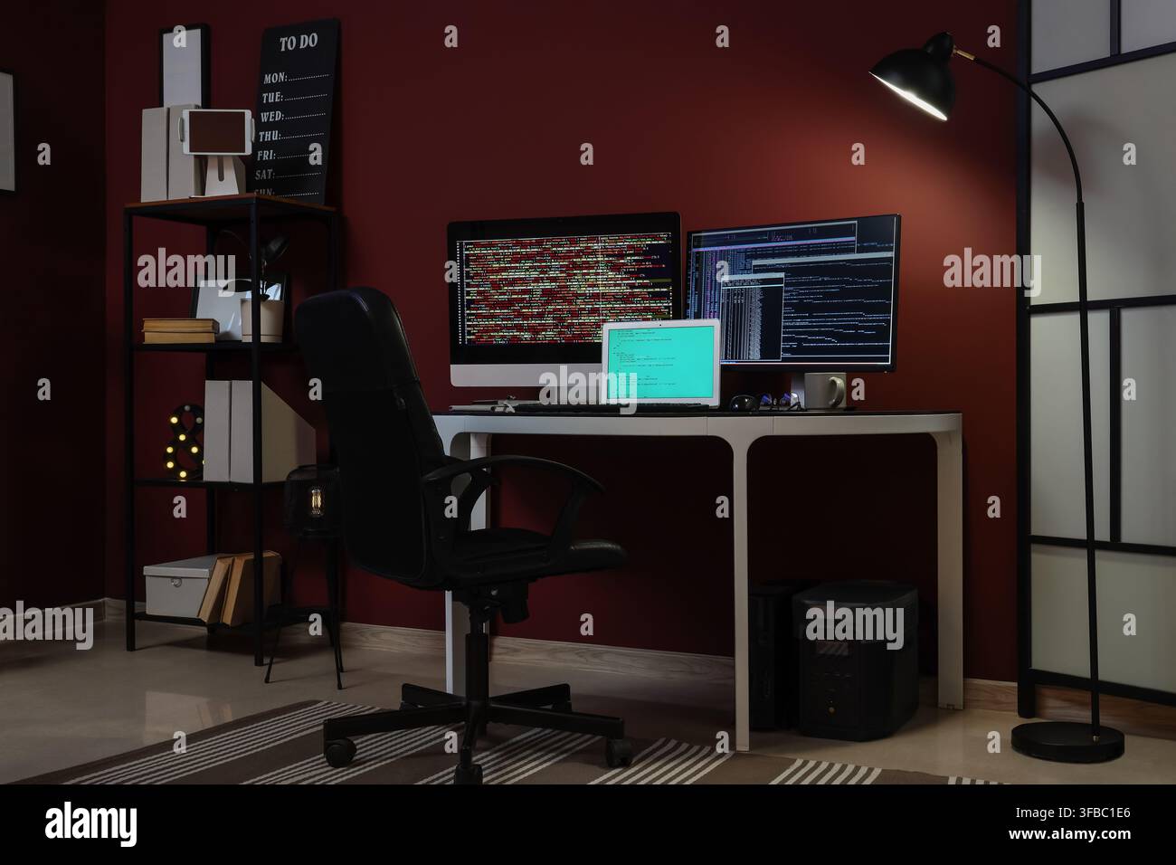 Remote work and coding late at night, empty home office desk with multiple screens showing programming code Stock Photo