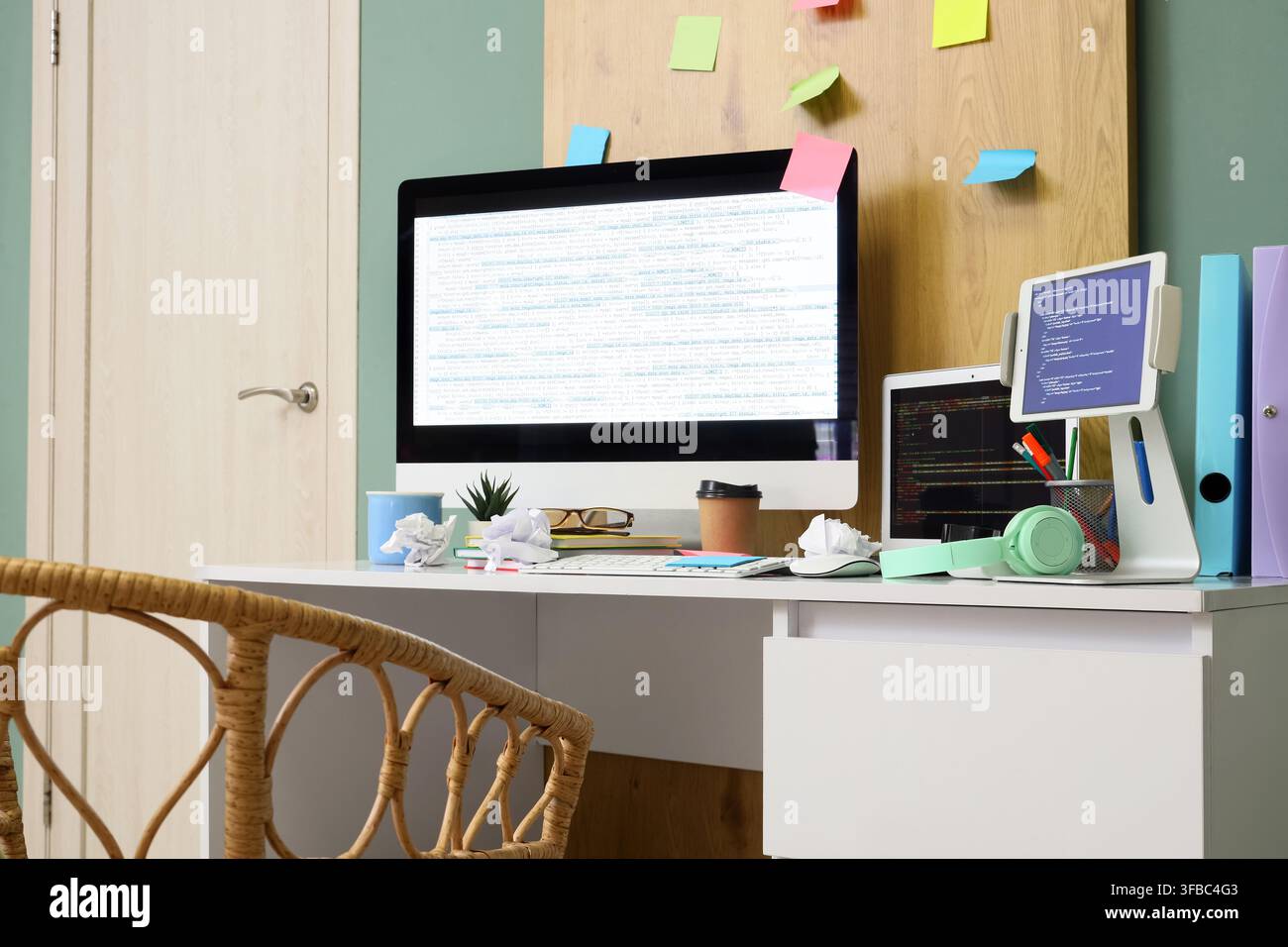 Software development and coding workspace, modern home office with multiple screens displaying code and sticky notes on a wooden board Stock Photo