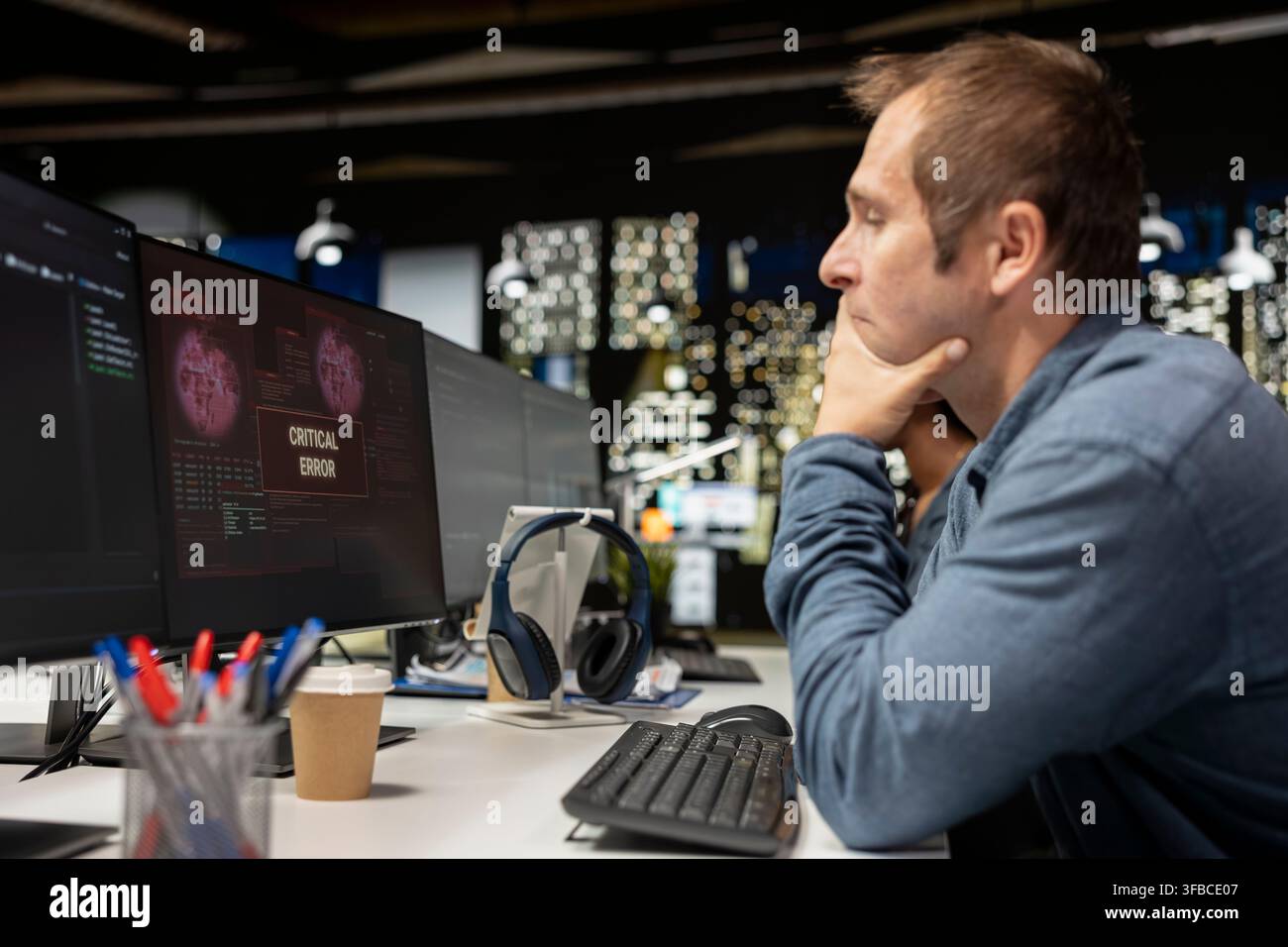 Programmer at office desk thinking how to fix critical error warning displayed on computer. Tech company IT employee brainstorming how to fix computer bug affecting server network Stock Photo