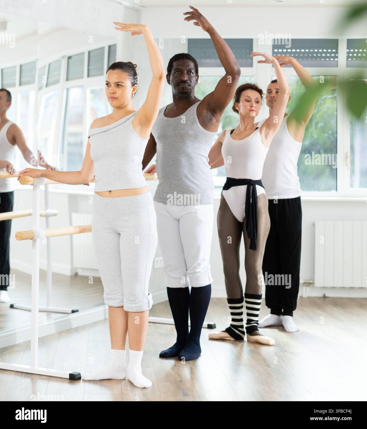 Group mastering third position at barre in ballet studio Stock Photo