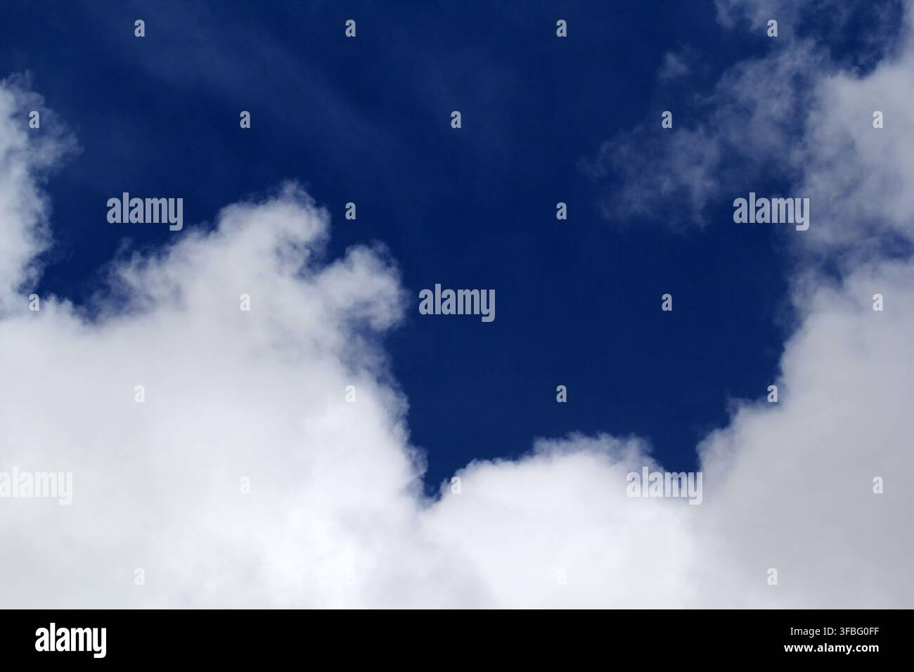 A vibrant, deep blue sky framed by fluffy white cumulus clouds on a bright, sunny day Stock Photo