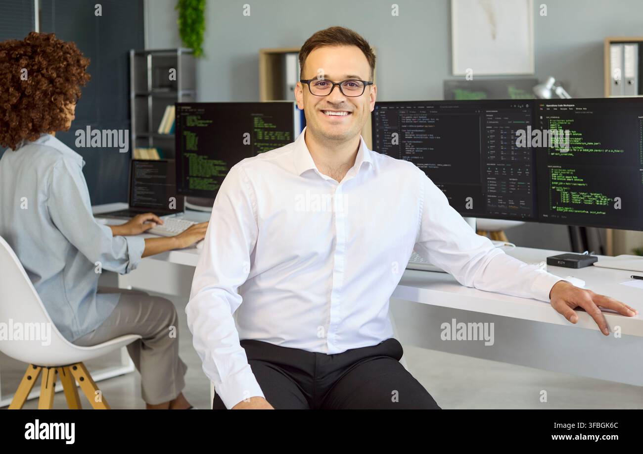 Smiling male programmer in office with code on monitors confident software engineer Stock Photo