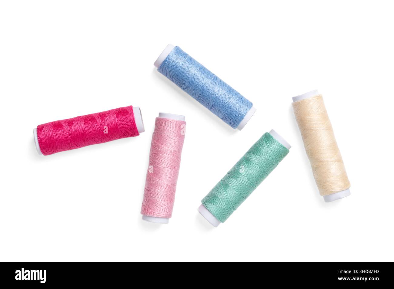 Five sewing thread spools, randomly distributed against a plain white background. Vibrant and colorful polyester sewing thread, wound onto paper rolls Stock Photo