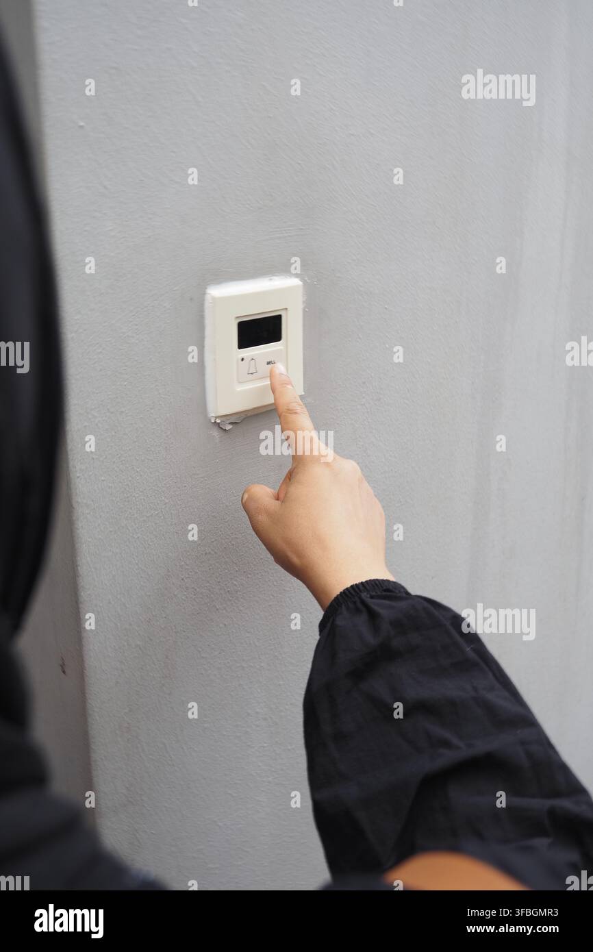 A hand presses a bell button on a wall Stock Photo