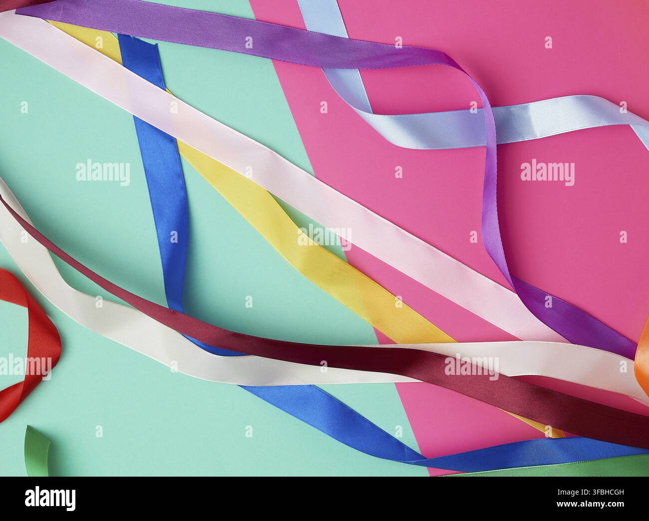 Many silk multi-colored ribbons on a colored background, top view Stock Photo